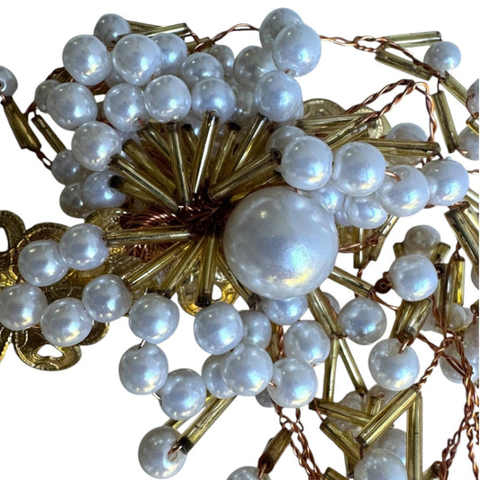 A close-up of a vintage-style brooch or hair ornament featuring a large iridescent white pearl surrounded by smaller white pearls, gold-toned metallic spikes, and gold-toned chain links on a white background.